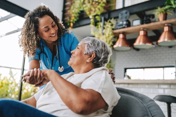 A caregiver leaning in warmly beside a smiling older woman during an activity at home